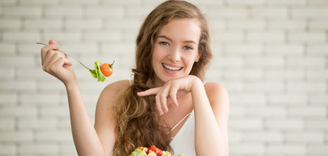 Young woman eating a fresh salad with vegetables and fruit for an ozone therapy aftercare