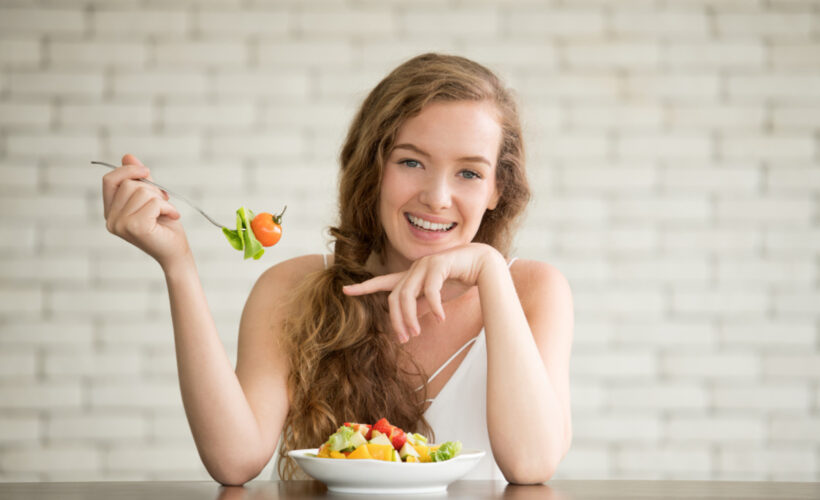 Young woman eating a fresh salad with vegetables and fruit for an ozone therapy aftercare