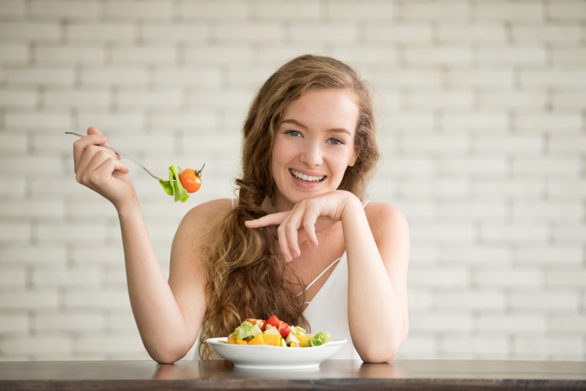 Young woman eating a fresh salad with vegetables and fruit for an ozone therapy aftercare