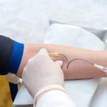 Gloved practitioner drawing blood from patient's arm as the first step of an ozone therapy detox autohemotherapy session