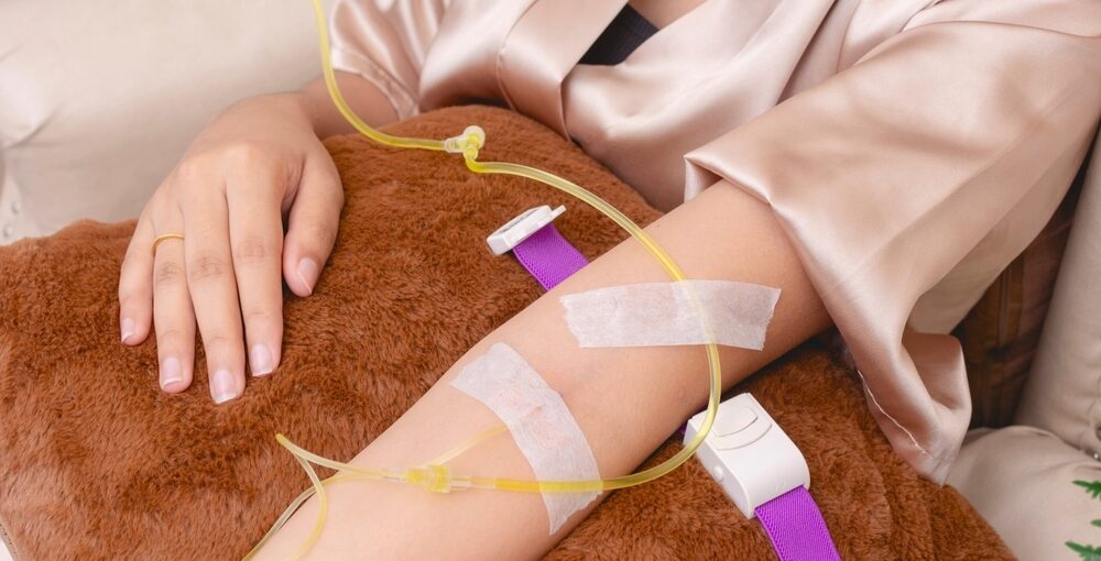 Woman in satin robe relaxing with an IV line in her forearm during a glutathione IV therapy session
