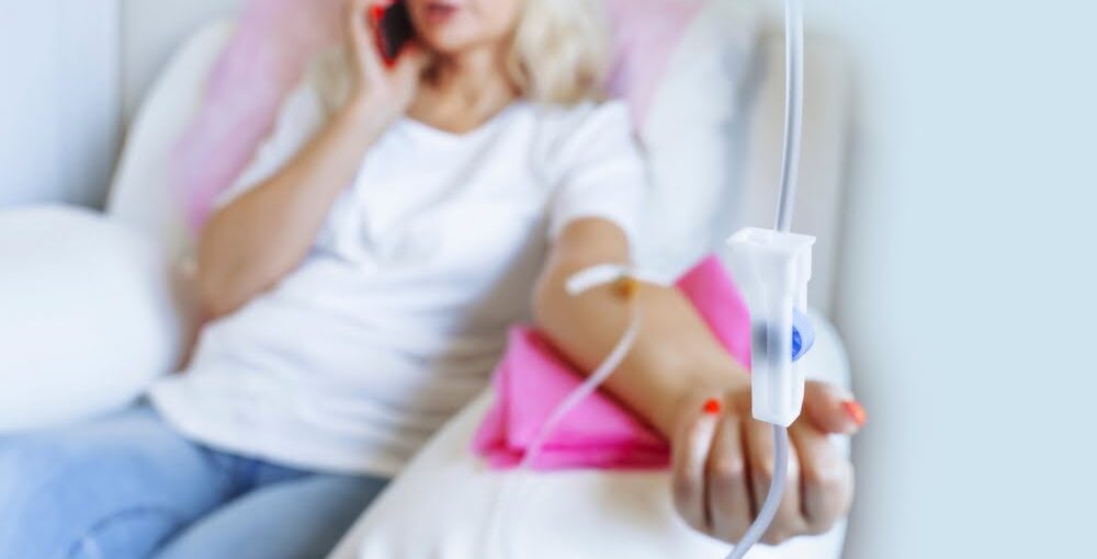 Woman relaxing and talking on phone while receiving an IV drip during an IV therapy for athletes recovery session