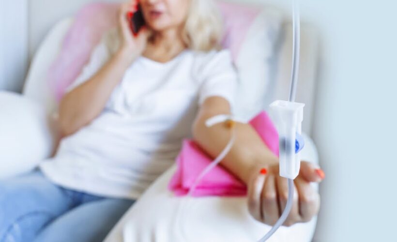 Woman relaxing and talking on phone while receiving an IV drip during an IV therapy for athletes recovery session