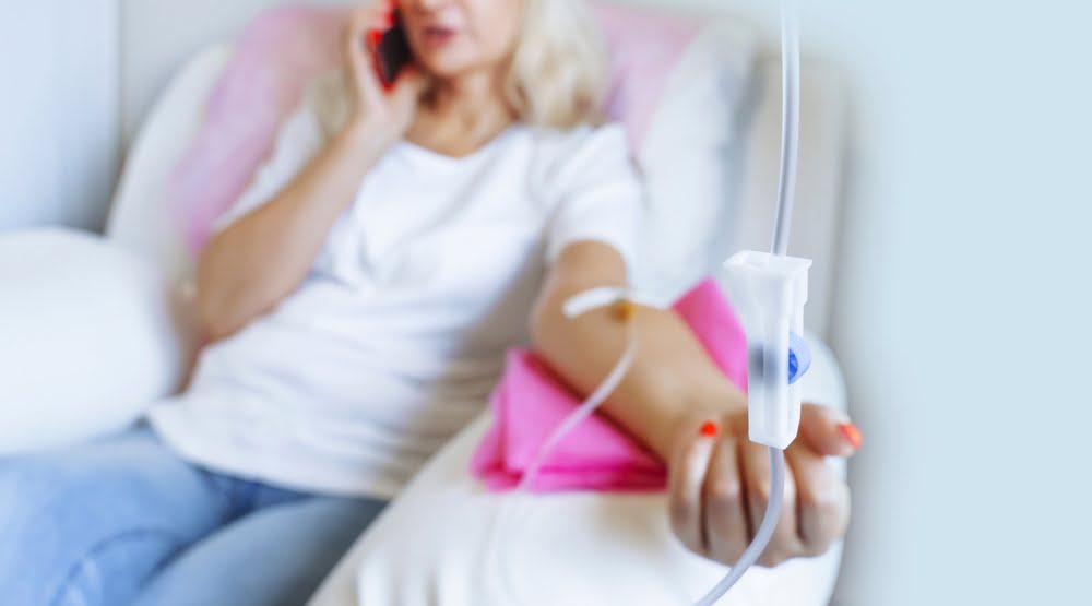 Woman relaxing and talking on phone while receiving an IV drip during an IV therapy for athletes recovery session