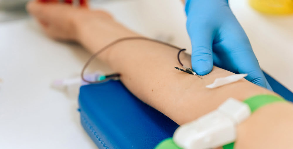 Gloved practitioner adjusting IV needle in patient's forearm during an ozone therapy for fatigue autohemotherapy session