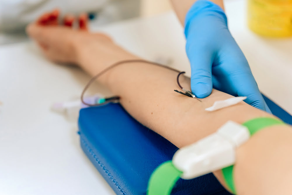 Gloved practitioner adjusting IV needle in patient's forearm during an ozone therapy for fatigue autohemotherapy session