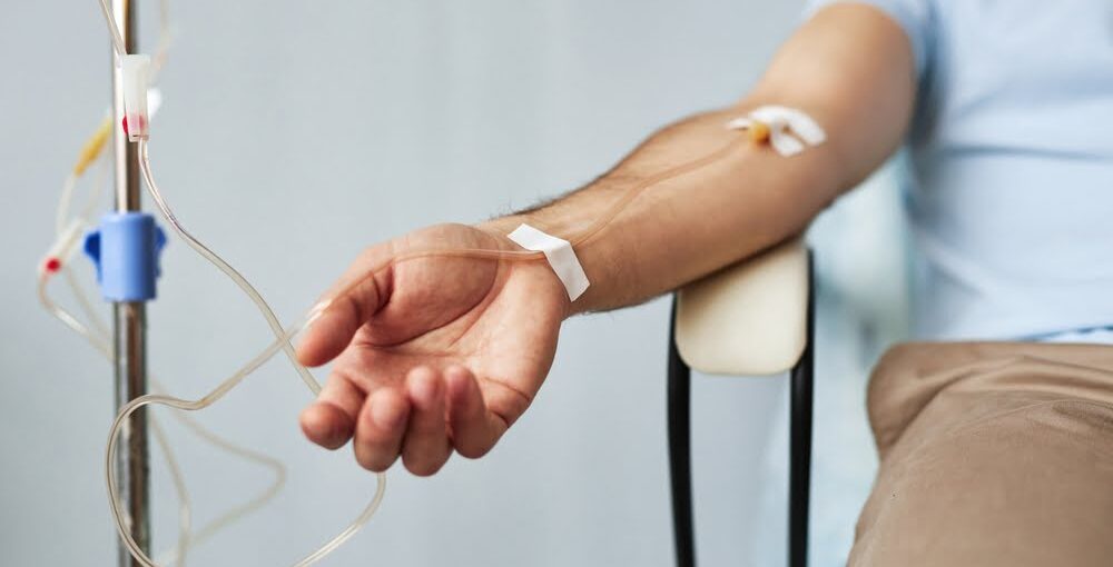 Male patient sitting with an IV line in his forearm during an IV therapy for immune support session in a clinical wellness setting