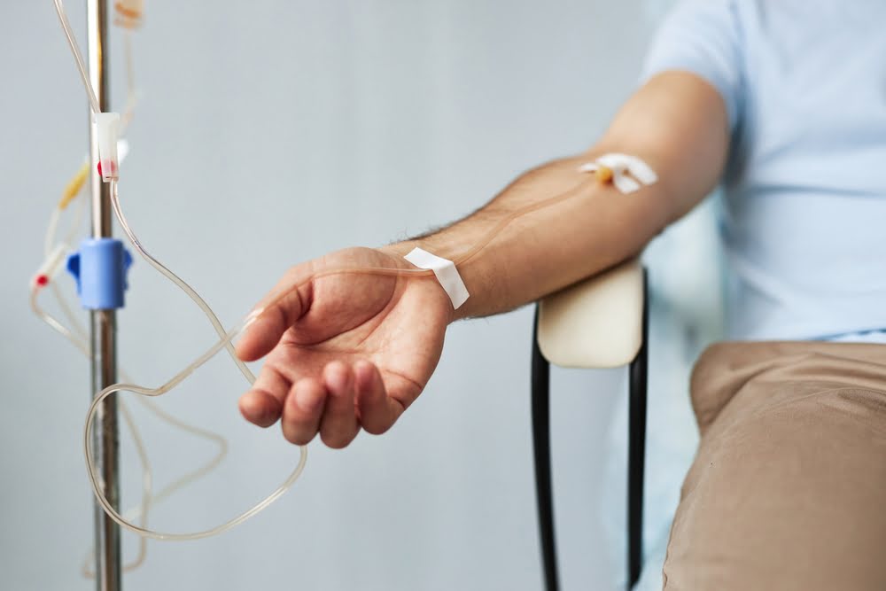 Male patient sitting with an IV line in his forearm during an IV therapy for immune support session in a clinical wellness setting