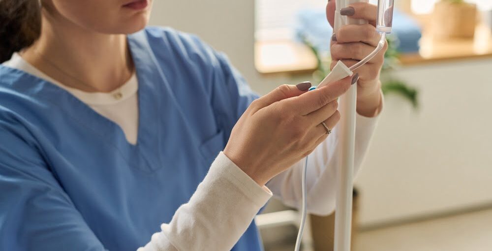 Female practitioner in blue scrubs carefully preparing an IV drip line for a Myers cocktail IV session in a wellness clinic