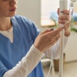 Female practitioner in blue scrubs carefully preparing an IV drip line for a Myers cocktail IV session in a wellness clinic
