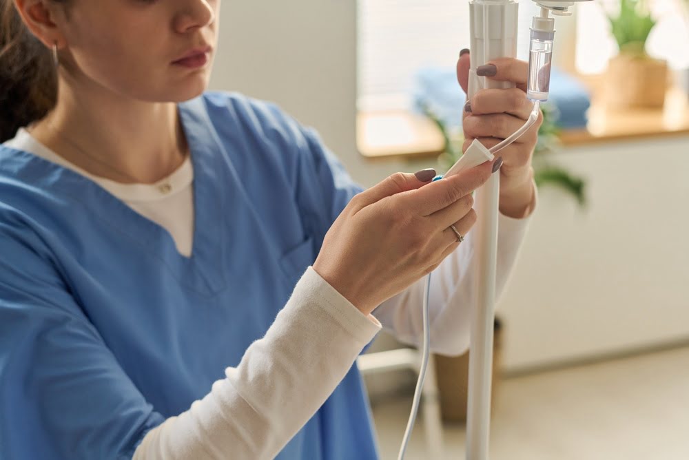 Female practitioner in blue scrubs carefully preparing an IV drip line for a Myers cocktail IV session in a wellness clinic