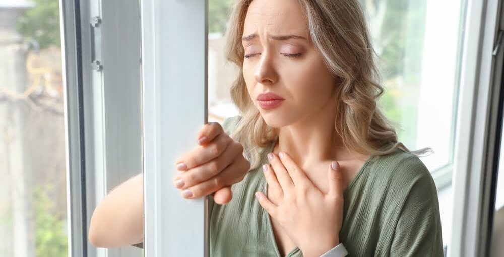 Woman standing by a window with hand on chest experiencing anxious distress, representing the biological and emotional burden that ozone therapy for anxiety aims to address