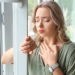 Woman standing by a window with hand on chest experiencing anxious distress, representing the biological and emotional burden that ozone therapy for anxiety aims to address