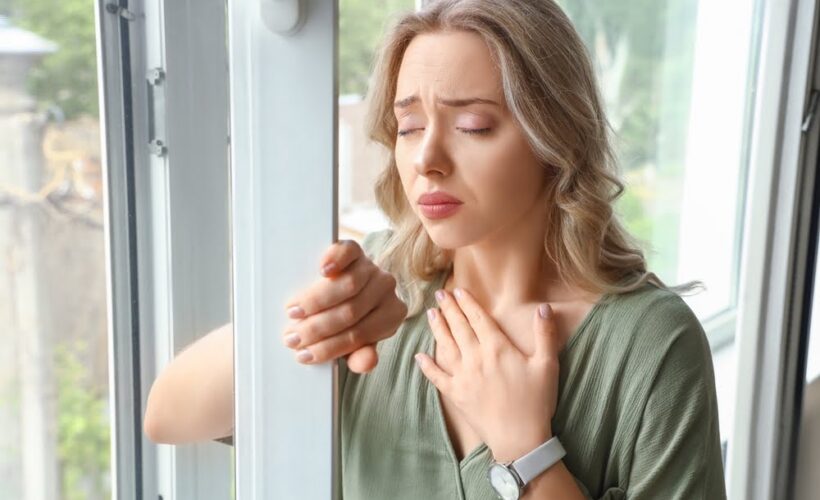 Woman standing by a window with hand on chest experiencing anxious distress, representing the biological and emotional burden that ozone therapy for anxiety aims to address