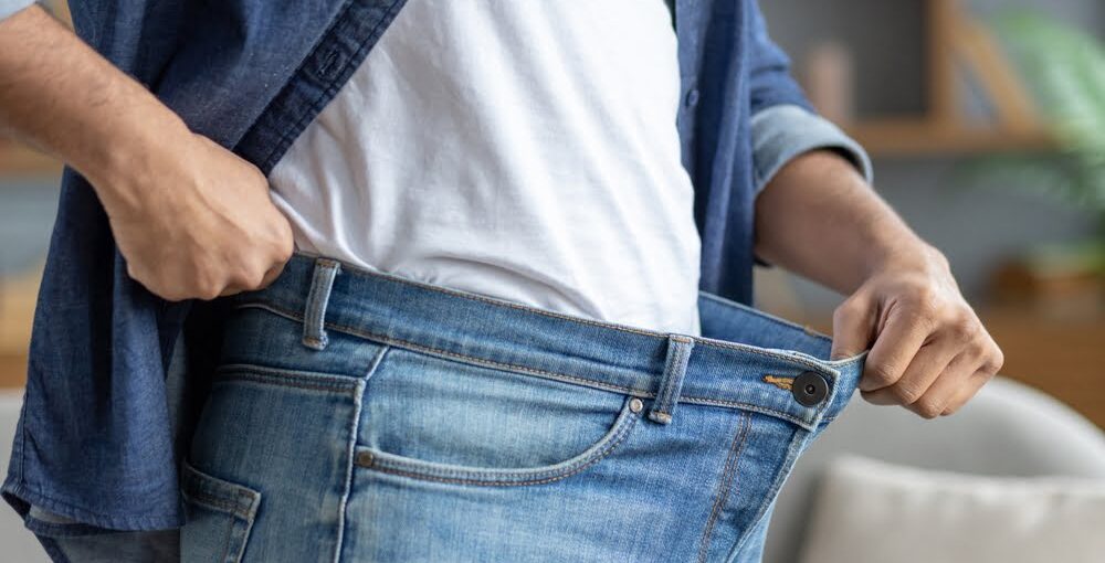 Person holding open oversized jeans waistband showing weight loss progress supported by an ozone therapy for weight loss and metabolic wellness protocol