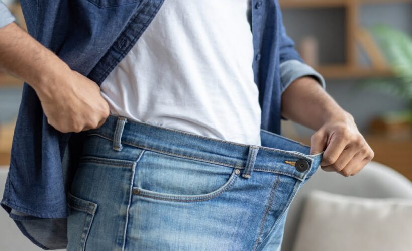 Person holding open oversized jeans waistband showing weight loss progress supported by an ozone therapy for weight loss and metabolic wellness protocol