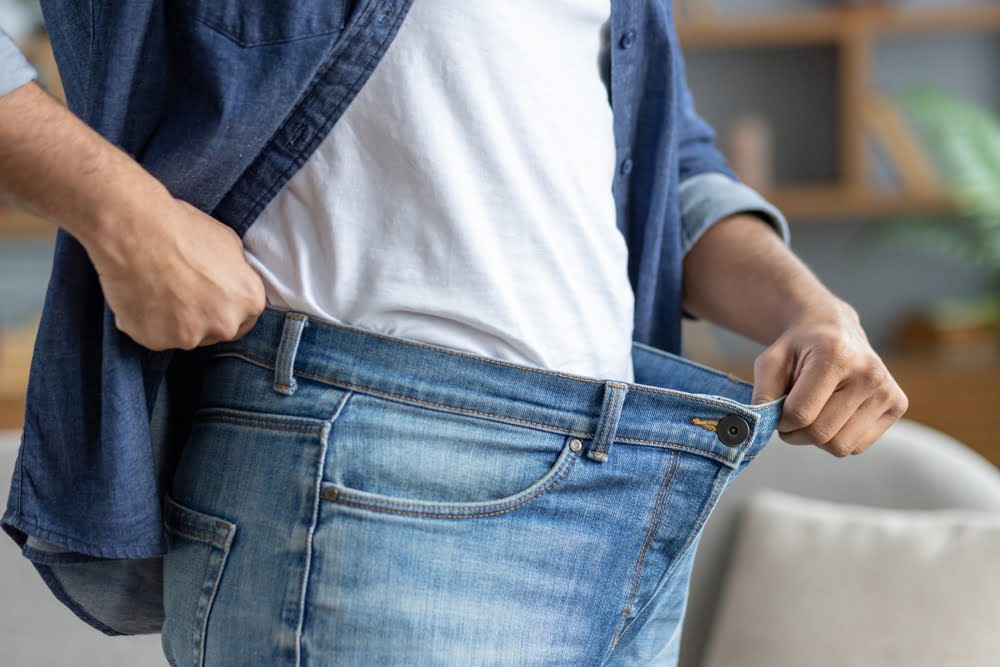 Person holding open oversized jeans waistband showing weight loss progress supported by an ozone therapy for weight loss and metabolic wellness protocol